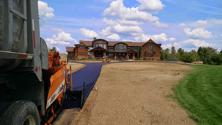 Orange paver laying residential driveway toward a large home under construction