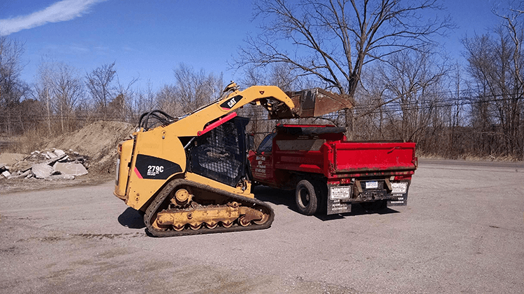 CAT 279C skid steer loading a red dump truck with debris